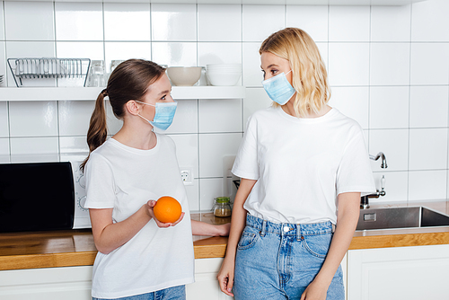 young woman in medical mask holding orange near sister