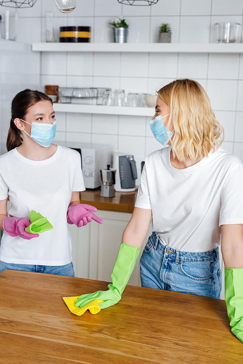 sisters in medical masks and latex gloves holding rags while looking at each other