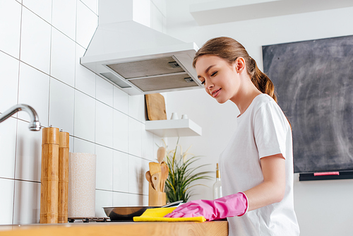 selective focus of happy woman in pink rubber glove cleaning kitchen
