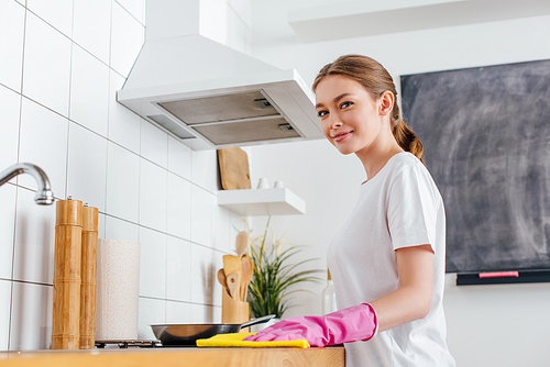 selective focus of cheerful woman in pink rubber glove cleaning kitchen