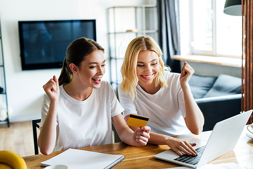 cheerful sisters online shopping near laptop at home