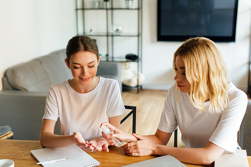 woman holding bottle with hand sanitizer near cheerful sister at home