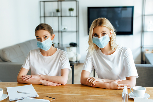 sisters in medical masks near credit card and cups on table