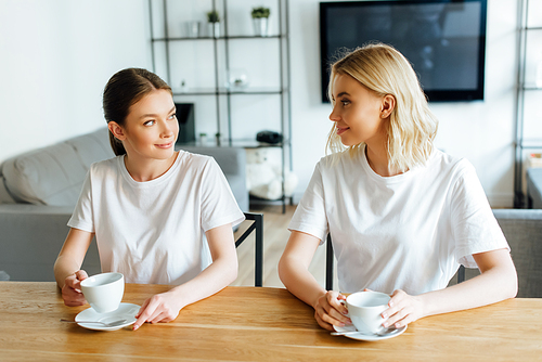 attractive sisters looking at each other while holding cups of coffee