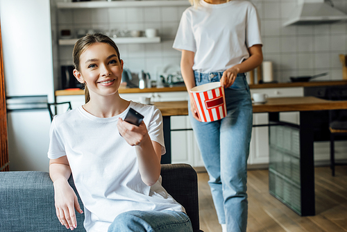 selective focus of happy girl holding remote controller near sister with tasty popcorn