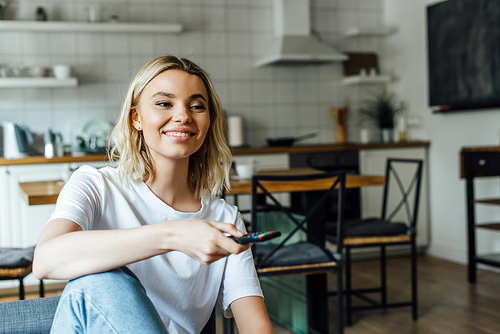 Beautiful smiling woman clicking channels on sofa at home