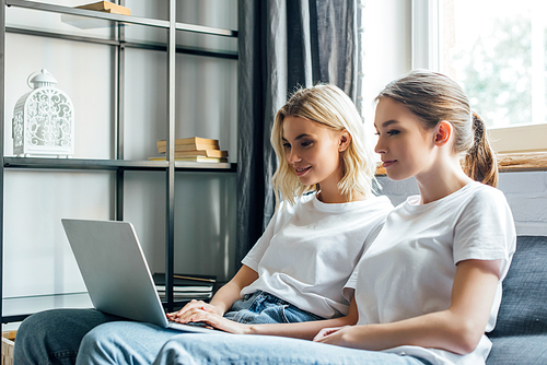 Selective focus of sisters using laptop on couch at home