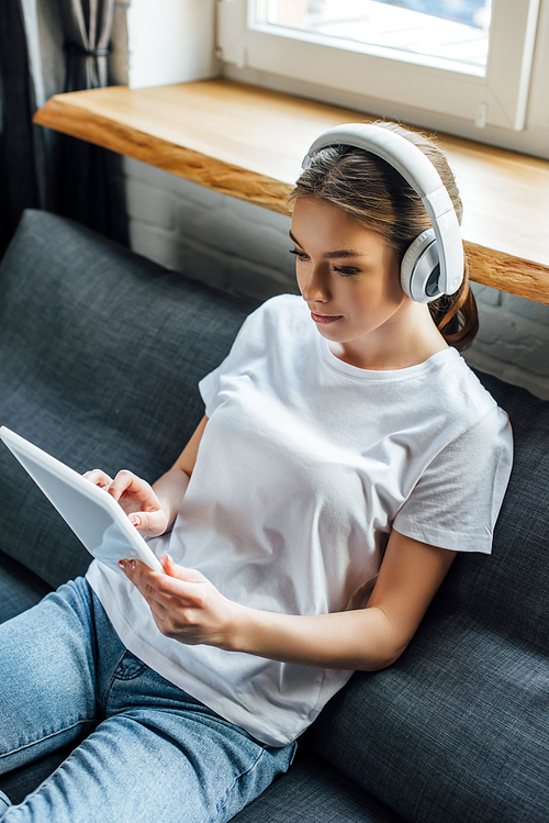 Attractive girl in headphones using digital tablet in living room