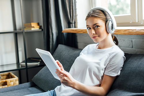 Attractive woman in headphones  while using digital tablet on sofa