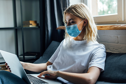 Young woman in medical mask using laptop at home