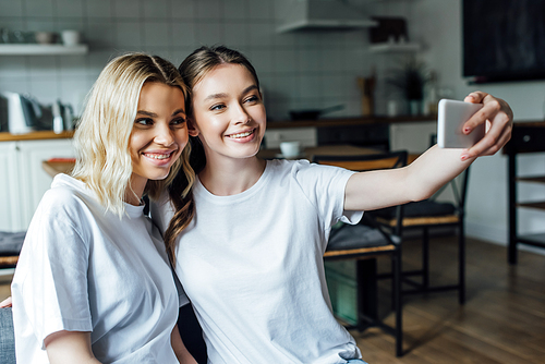 Beautiful smiling sisters taking selfie with smartphone at home