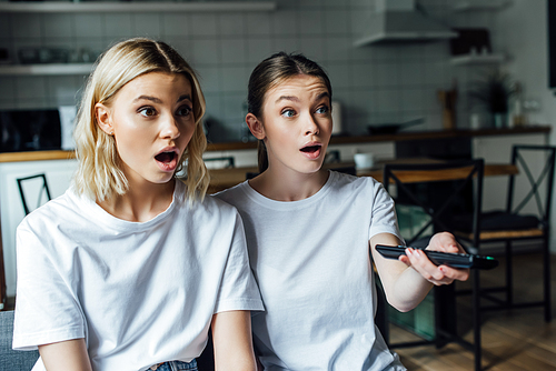Excited sisters clicking channels on couch at home