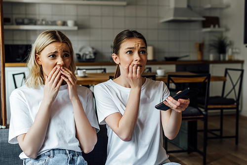 Shocked and scared sisters watching tv on couch at home