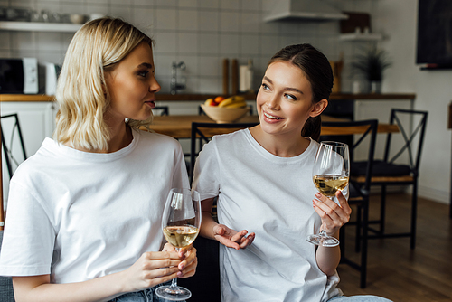 Smiling sisters talking while holding glasses of wine at home