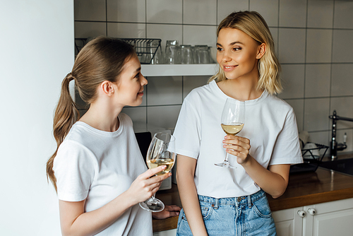Smiling sisters holding glasses of wine in kitchen