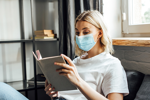 Blonde woman in medical mask reading book at home