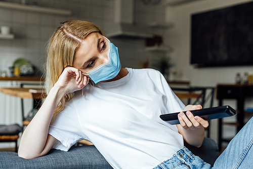 Blonde girl in medical mask watching movie in living room