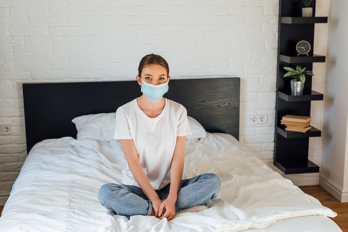 Young woman in medical mask  while sitting on bed