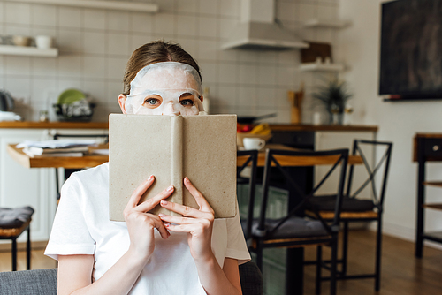 Young woman in face mask  while holding book at home
