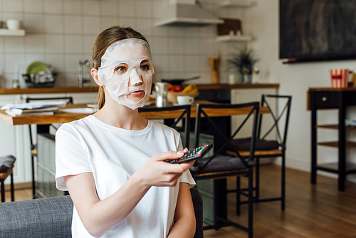 Young woman in face mask holding remote controller at home