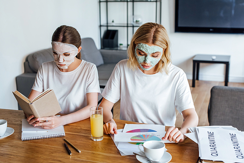Sisters in face masks reading book and working with papers at table