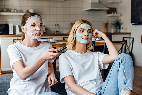 Sisters in face masks watching tv on couch at home