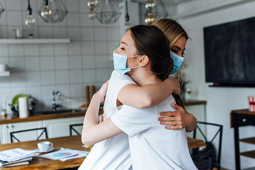 Side view of sisters in medical masks embracing at home