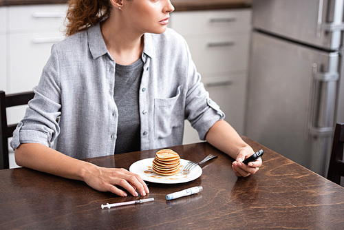 cropped view of woman with diabetes holding glucose monitor near pancakes