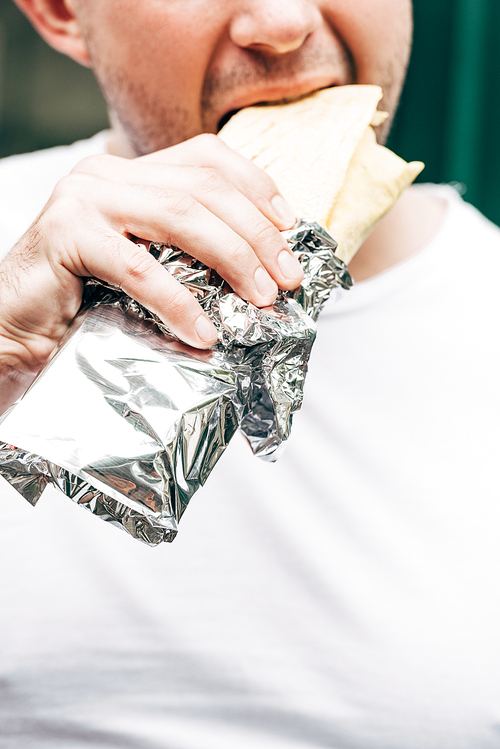 cropped view of man eating doner kebab in aluminium foil