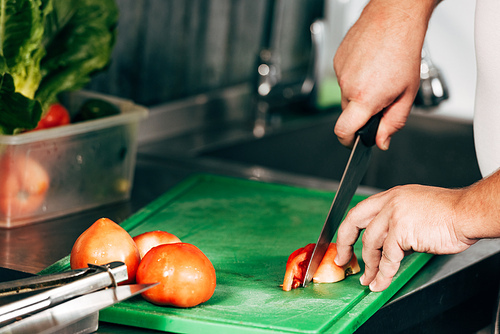 cropped view of cook cutting tomatoes on chopping board
