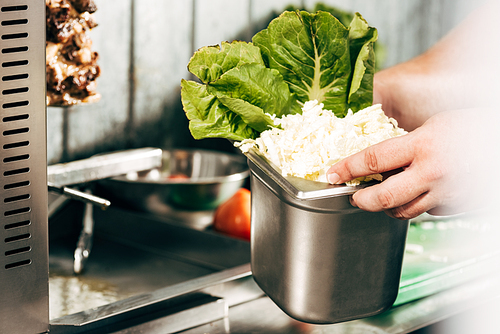 cropped view of cook holding container with cut lettuce