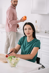 happy disabled woman  while cutting tomatoes in kitchen near boyfriend holding bell pepper