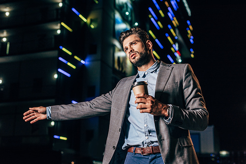handsome businessman in formal wear hitching and holding paper cup in night city