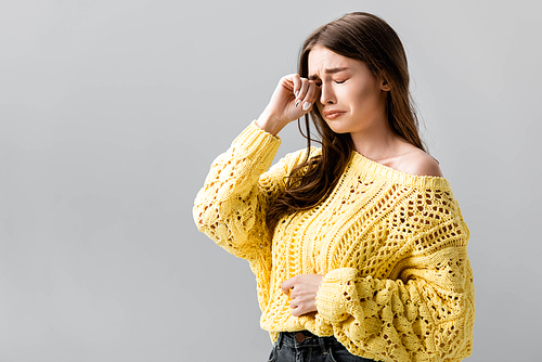 unhappy girl in yellow sweater crying and wiping tears with hand isolated on grey