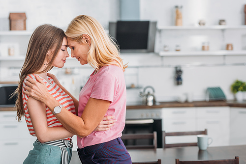 happy mother and daughter embracing while standing face to face in kitchen