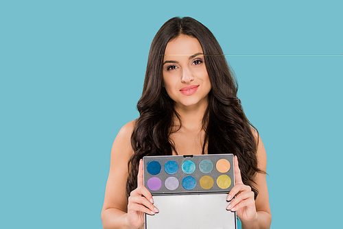 cheerful woman holding eye shadow palette isolated on blue