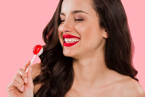 cheerful girl looking at sweet lollipop isolated on pink