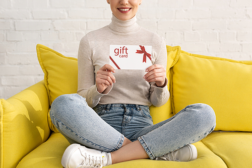 Cropped view of smiling woman showing gift card on sofa