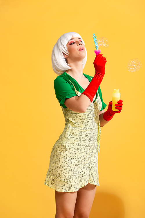 beautiful pop art girl in white wig blowing soap bubbles, on yellow