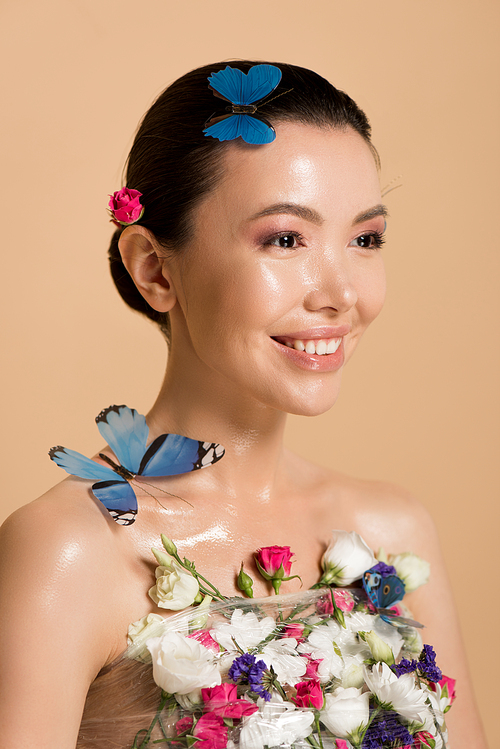 smiling naked asian girl in flowers with butterflies on body isolated on beige