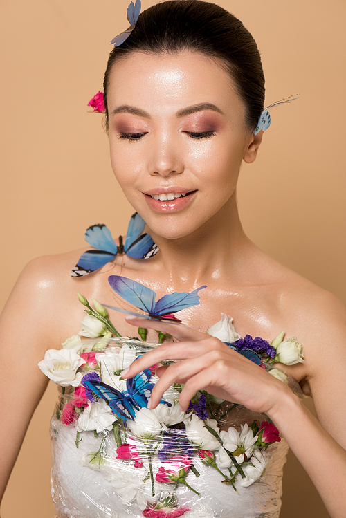 beautiful happy naked asian girl in flowers with butterflies on hand on beige