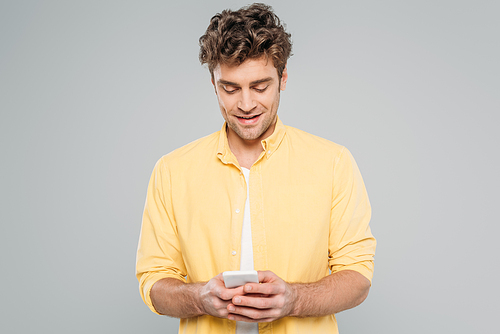 Front view of man smiling and chatting on smartphone isolated on grey