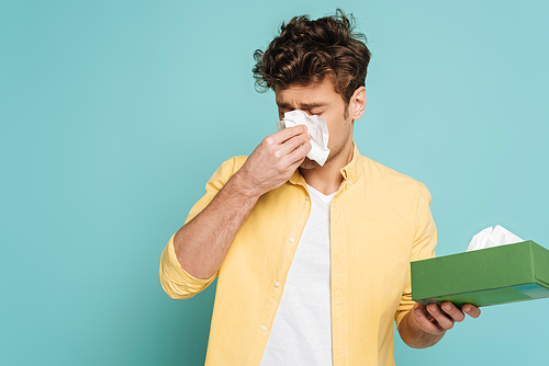 Man holding box with napkins and blowing out nose isolated on blue