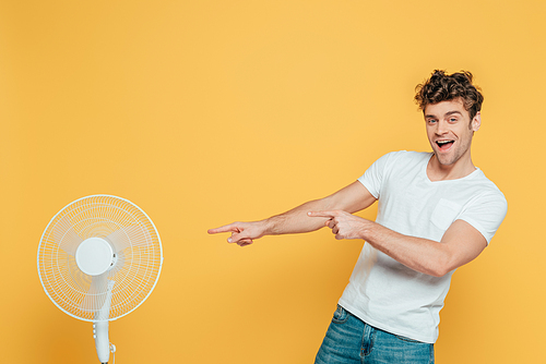 Excited man  and pointing at electric fan isolated on yellow