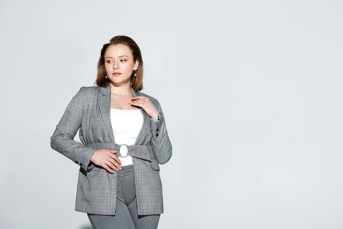 beautiful, serious overweight girl touching chest while posing on grey