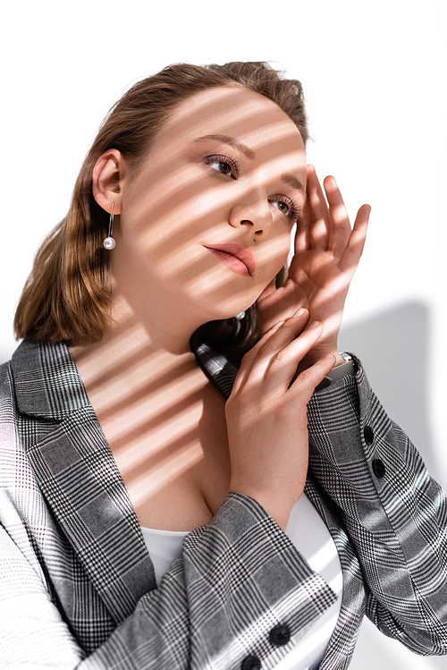 dreamy, beautiful overweight girl holding hands nearf face while posing on white in sunlight with shadows