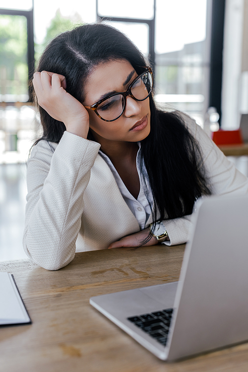 selective focus of tired businesswoman in glasses looking at laptop