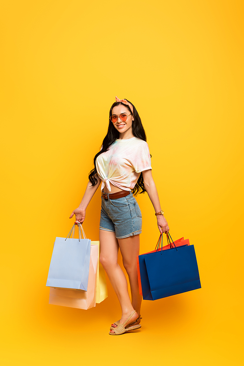 smiling stylish summer brunette girl with shopping bags on yellow background