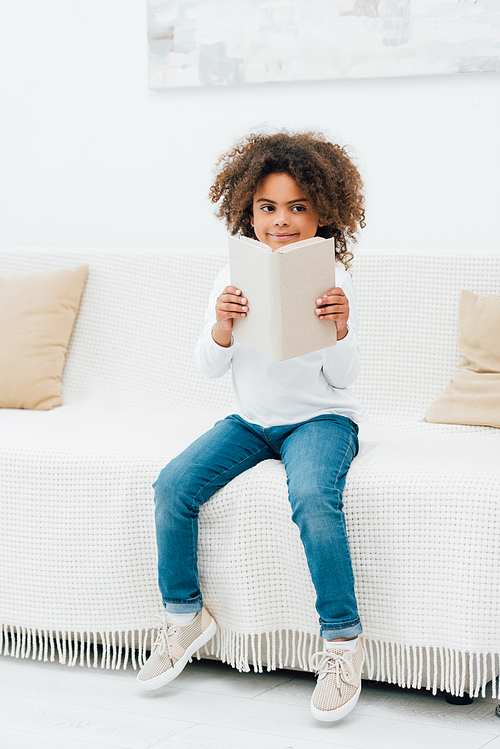 african american kid sitting on sofa and holding book