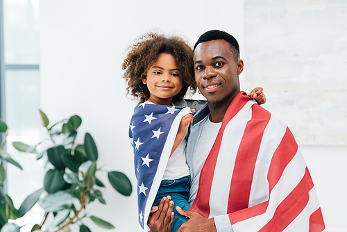 african american father and daughter covered with flag of america 